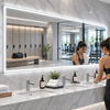 Large illuminated LED mirror with digital clock and touch controls above a double vanity in a modern gym bathroom.